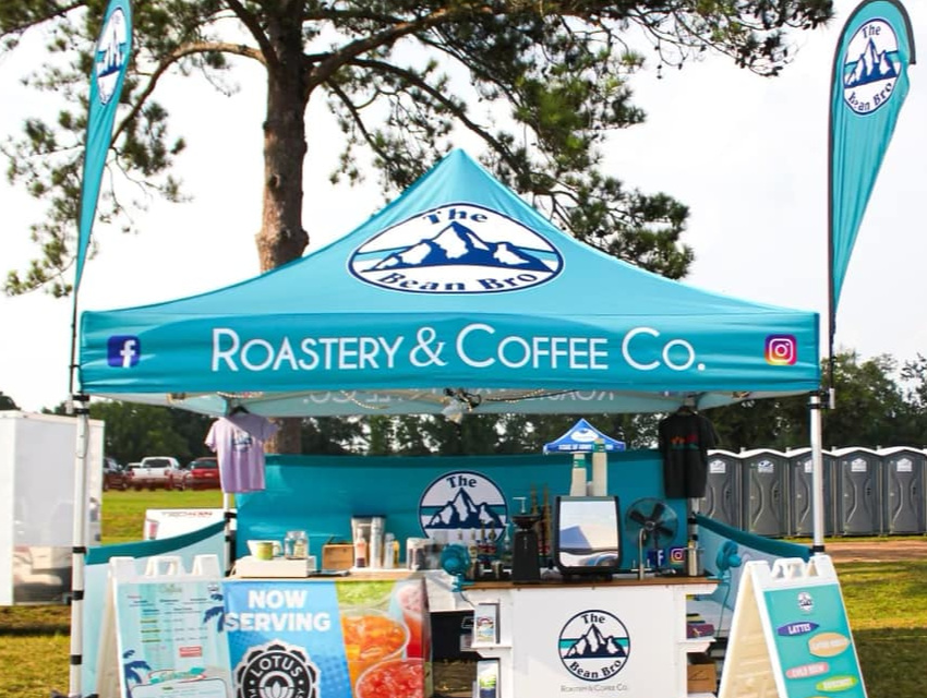 The Bean Bro Roastery & Coffee Co custom 10x10 coffee tent with cyan canopy and branded flags at an outdoor festival
