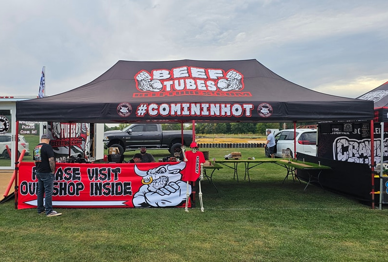 Custom pop up tent with logo for Beef Tubes featuring a large branded canopy, table banner, and surrounding flags at an outdoor event.