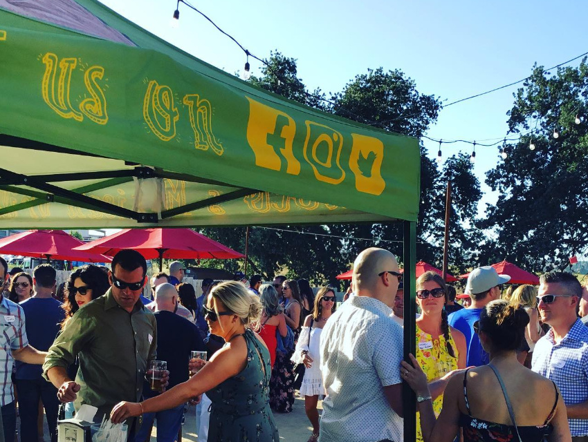 Festival attendees gathered at Choco’s Mexican Grill booth enjoying food and conversation under a green canopy
