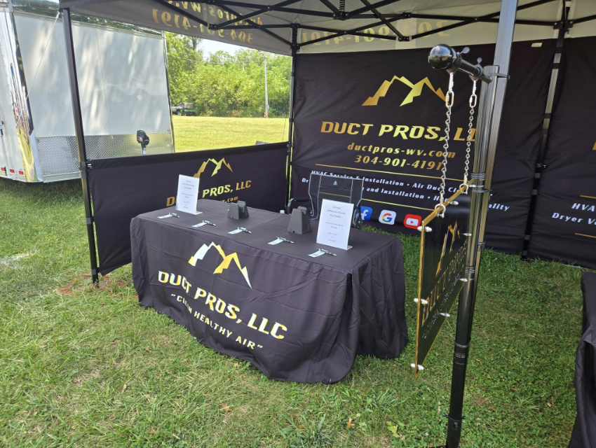 Duct Pros custom tent showing full back wall and half-height side walls with branded table covers