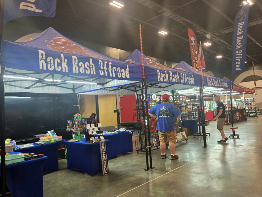 Rock Rash Offroad trade show setup featuring tall branded feather flags and a custom canopy that creates a visible, high-impact presence across the event floor.