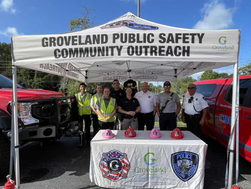 Groveland Public Safety team standing under their custom tent with branded table cover and red fire helmets displayed for kids