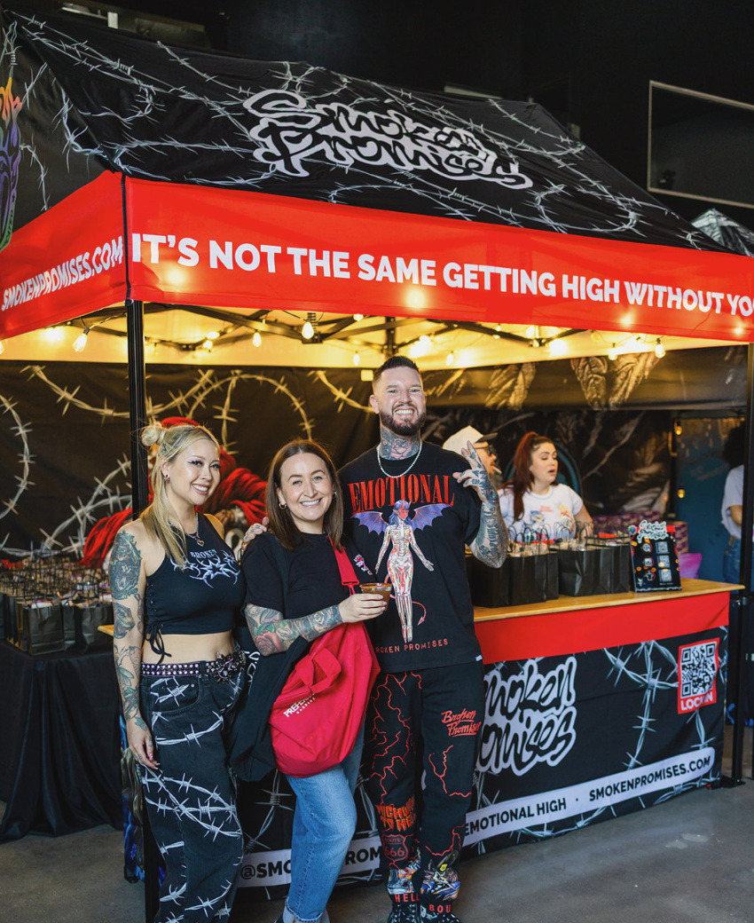 Smoken Promises team standing in front of their custom Cabin canopy vendor booth at an indoor event
