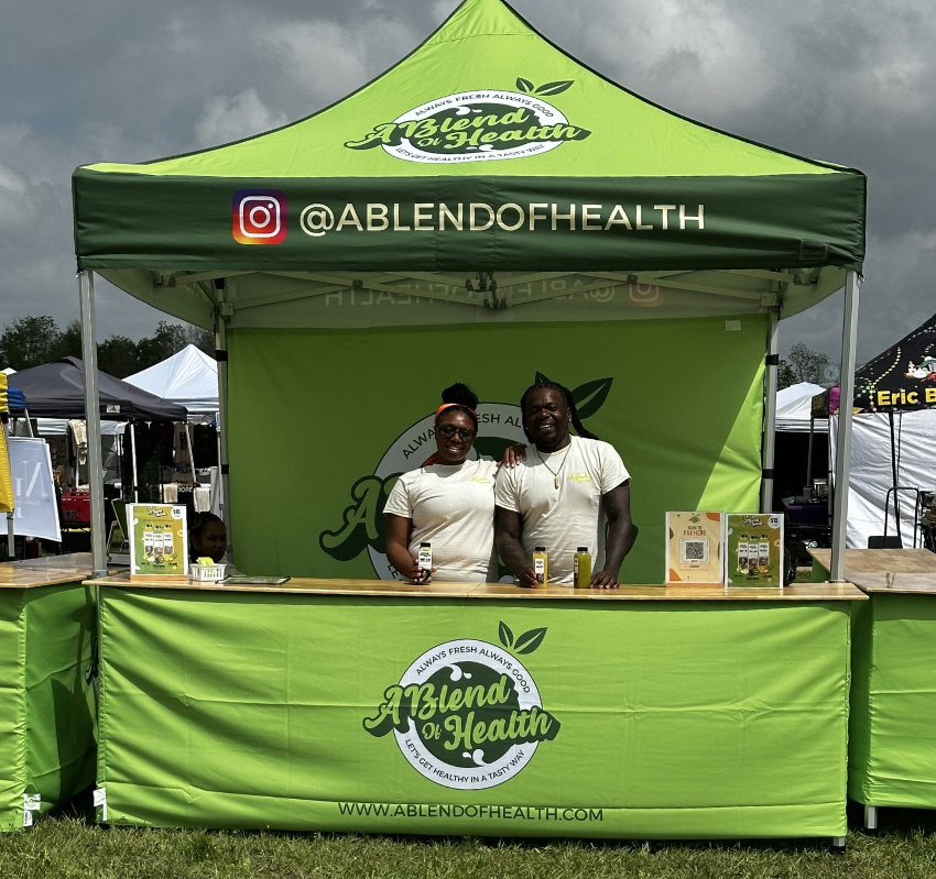 Vendor Pro tent setup for A Blend of Health with clean green branding, printed back wall, and organized aluminum counters