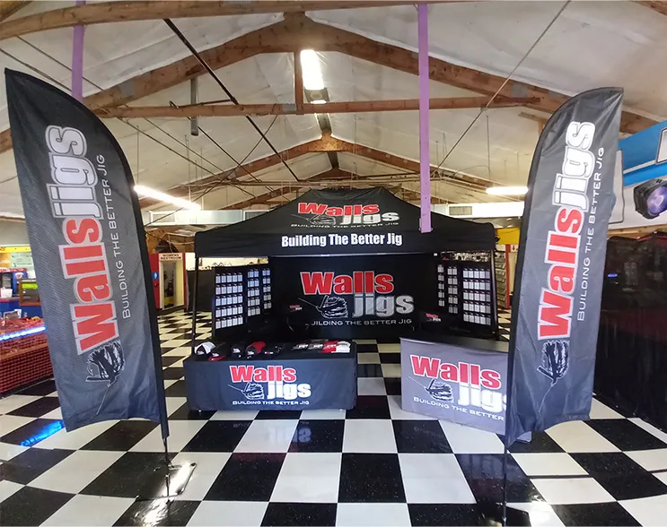 Walls Jigs indoor trade show booth with matching feather flags and a custom printed canopy, creating a unified and eye-catching display.